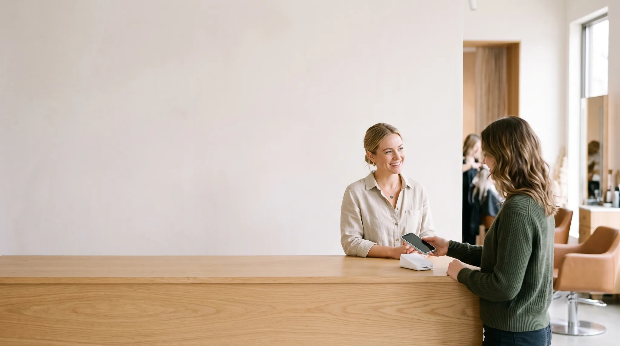 Salon owner at the front desk while a customer taps a phone on the payment terminal